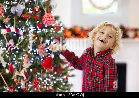 Enfant decorant arbre de Noel a la maison. Petit garcon dans une chemise a carreaux avec ornement de Noel. La famille avec les enfants celebrent les vacances d hiver. Les enfants decorent le