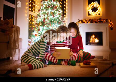 Enfants à l'arbre de Noël et cheminée sur veille de Noël. Famille avec enfants célébrer Noël à la maison. Garçon et fille en pyjama noël décoration correspondant Banque D'Images