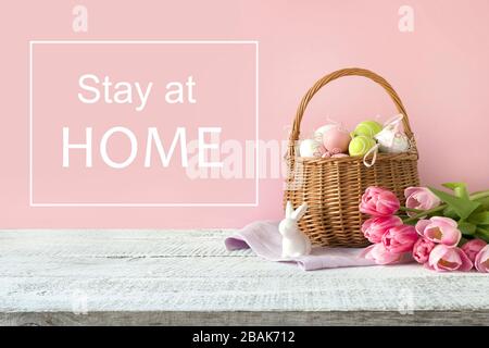 Panier en osier avec œufs de pâques et tulipes roses. Printemps fond rose de pâques. Slogan - séjour à la maison. Banque D'Images