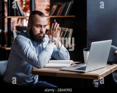 Homme d'affaires barbu dans un costume travaille derrière l'ordinateur portable assis dans un collègue de bureau confortable. Banque D'Images