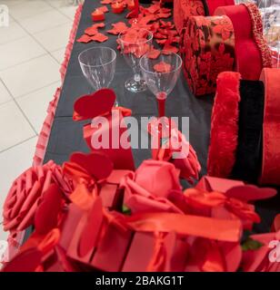 Gros plan de feuilles de rose rouge imitation ou artificielle, boîtes en forme de coeur rouge et verres à vin fond. Mise au point sélective. Banque D'Images