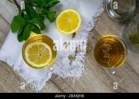 Tasse transparente en verre avec support à thé à la menthe sur un support en bois, à côté d'un bol à sucre avec des cubes de sucre, des feuilles de citron et de menthe tranchées Banque D'Images