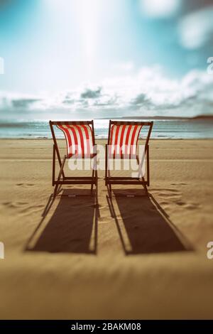 Deux chaises longues rouges et blanches solitaires sur une plage déserte, avec une tempête approchant. Banque D'Images