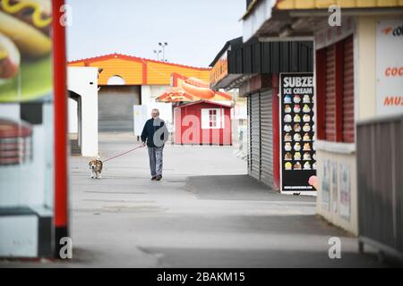 Porthcawl, Pays de Galles du Sud. 28 mars 2020. Un homme marche seul avec son chien à travers les étals fermés de Porthcawl dans le sud du Pays de Galles, alors que le Royaume-Uni est en train de s'arrêter et des mesures de distanciation sociale sont mises en place pour essayer de combattre la pandémie de Coronavirus. Crédit : Robert Melen/Alay Live News. Banque D'Images