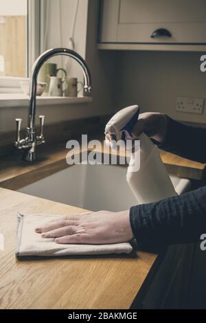 Un gros plan d'une paire de mains humaines nettoyant l'intérieur d'une cuisine avec un spray antibactérien et un chiffon pour désinfecter les surfaces de travail pendant le Cor Banque D'Images