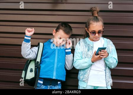 Les enfants souriants aiment écouter de la musique sur smartphone sur fond marron Banque D'Images