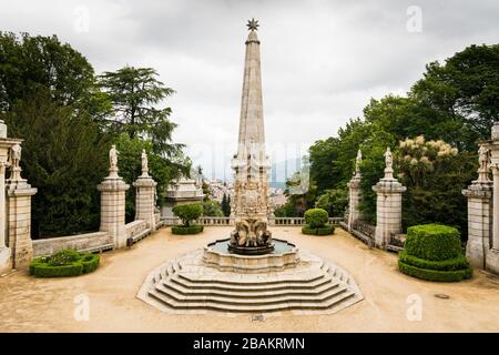 Belle cour avec une vieille fontaine ornée et obélisque entouré de statues classiques et de verdure au-dessus de la ville de Lamego, Portugal sous Banque D'Images