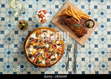 Viande, pomme de terre, légumes, pizza et côtes de porc avec plat sur une table Banque D'Images