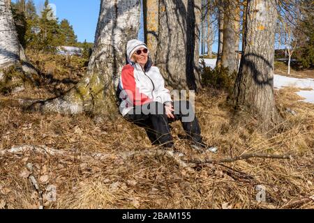 Les femmes matures au printemps assis sur le sol contre un arbre dans avec un sourire dans son visage et un ciel bleu en arrière-plan, photo de Mellansel, Suède. Banque D'Images