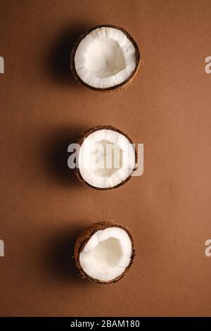 Trois fruits de coco en rangée sur fond brun Uni, concept abstrait de nourriture tropicale, vue de dessus Banque D'Images