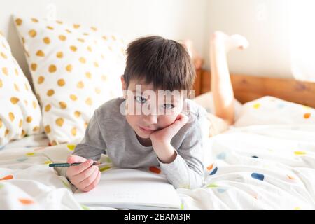 École Boy sur le lit et faire des devoirs à la maison, écrire dans le bloc-notes. Formation à distance en ligne. Quarantaine Banque D'Images