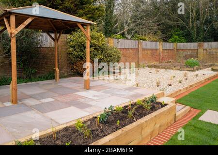 Un nouveau patio surélevé avec un belvédère en bois devant un lit fleuri surélevé et un jardin en gravier. Banque D'Images