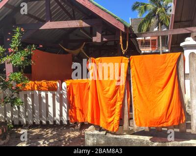 Vêtements de couleur orange blanchisserie des Monks bouddhistes du Laos se séchant sur la clôture blanche du temple, Luang Prabang, République du Laos Banque D'Images