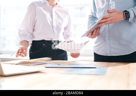 Gros plan de collègues non reconnaissables se tenant à la table et en discutant des documents financiers au bureau Banque D'Images