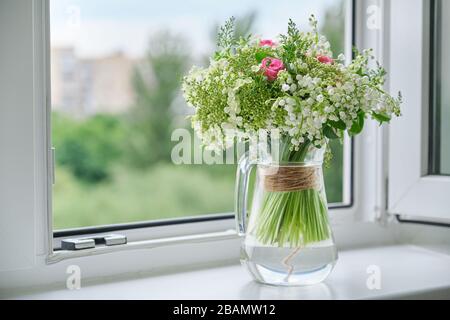 Printemps, bouquet de nénuphars frais de printemps de la vallée, roses roses, viburnum fleuri. Bouquet dans une verseuse en verre sur le seuil de fenêtre, fond de fenêtre ouvert Banque D'Images