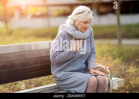 Femme senior souffrant de douleur lorsqu'elle est assise sur le banc Banque D'Images