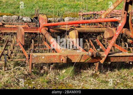 Gros plan sur un vieux cultivateur rouge et rouillé utilisé pour cultiver des terres agricoles Banque D'Images