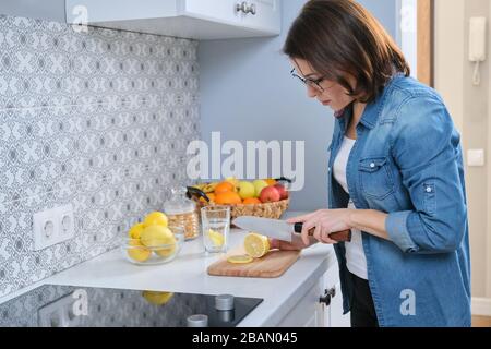 Femme coupant le citron avec couteau sur la planche à découper dans la cuisine. Banque D'Images