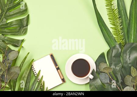 Tasse à café, carnet, stylo et feuille tropicale sur fond vert. Banque D'Images