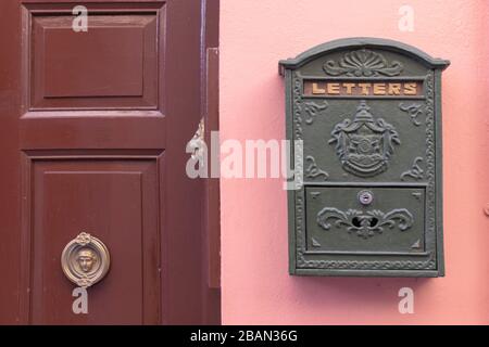 Boîte aux lettres verte, rétro et lumineuse, apposée sur le mur extérieur d'une maison rose. Il y a une porte marron avec bouton de porte doré Banque D'Images