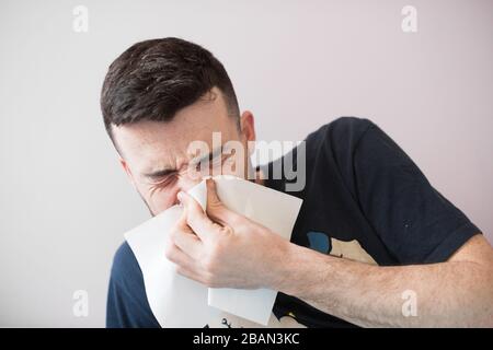 Jeune homme malade avec hanky. Guy éternuer. Il tient une serviette près de son nez. T-shirt noir. Isolé sur fond clair. Banque D'Images