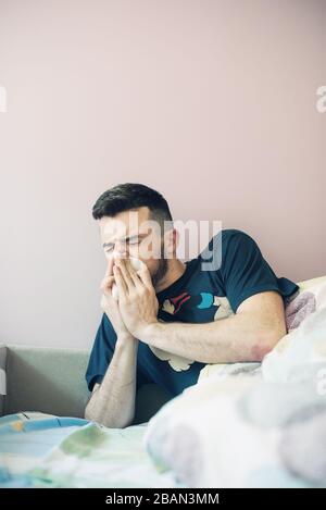 Jeune homme malade avec hanky. Guy allongé sur le lit. Il éternuise et tient une serviette près de son nez. Surfait d'une couverture. Isolé sur fond clair. Banque D'Images