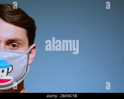 Gros plan d'un homme caucasien portant un drôle de masque de protection du visage de singe avec des yeux et des cheveux bruns, depuis la nouvelle éclosion de coronavirus. Banque D'Images