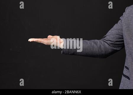 L'homme dans une veste tient un objet dans la paume de sa main sur un fond noir. Gros plan. Banque D'Images