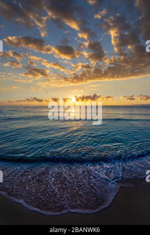 Magnifique paysage de nuages au lever du soleil sur la mer avec des vagues qui s'enroulent sur la plage de sable. Banque D'Images