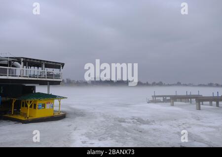 Une épaisse brume s'élève d'un lac gelé du Dow sur un matin chaud de printemps, obscurcissant le quai et la rive est. Ottawa (Ontario), Canada. Banque D'Images