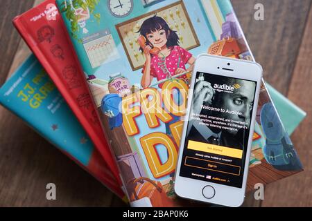 La page de connexion à l'application mobile Audible apparaît sur un smartphone au-dessus des livres de bibliothèque. Audible, propriété d'Amazon Inc., possède le plus grand catalogue de livres audio au monde. Banque D'Images