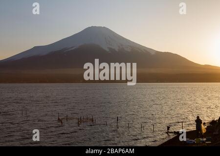 Un pêcheur, en silhouette, pose des filets au coucher du soleil sur le lac Yamanaka avec le Mont Fuji en arrière-plan Yamanashi, Japon. Banque D'Images