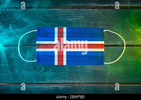 Masque médical pour la protection contre les maladies aéroportées, peint dans le drapeau national de l'Islande sur un fond noir dans la fumée bleu-vert. Prot. Médical Banque D'Images