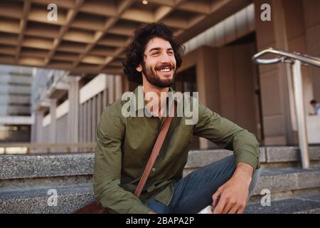 Beau jeune homme assis sur les escaliers tout en regardant loin Banque D'Images