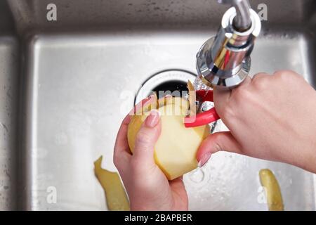 Vue rognée de la femme se décollait la pomme sur la machine de la décomposeuse de déchets alimentaires Banque D'Images