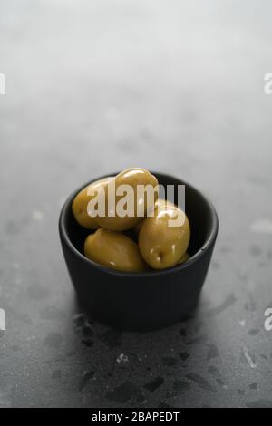 olives vertes géantes dans un bol noir sur une surface en béton Banque D'Images