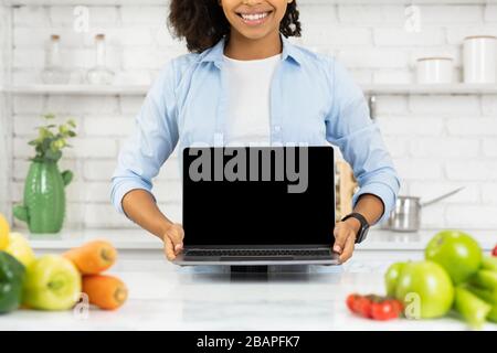 Une fille afro imreconnaissable tenant un ordinateur portable dans la cuisine Banque D'Images