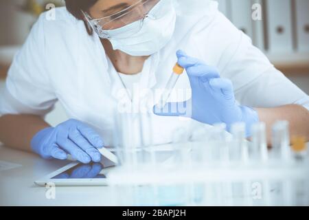 Scientifique professionnel de la femme dans les lunettes de protection et le masque faisant l'expérience avec des réactifs en laboratoire. Arrêt de la pandémie de coronavirus. Médecine Banque D'Images