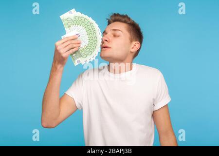 La cupidité et l'argent. Jeune homme d'affaires dans un t-shirt blanc décontracté qui sent les factures en euros avec expression de plaisir, en profitant de la vie riche, grand profit d'argent Banque D'Images