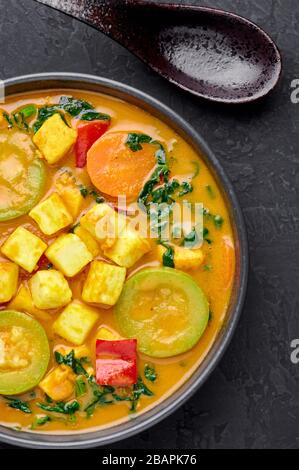 Une curry thaï de veau jaune avec tofu et légumes dans un bol noir à fond d'ardoise sombre. Curry thaïlandais végétarien avec tofu, courgettes, poivron, spina Banque D'Images