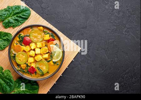 Veau jaune curry thaïlandais avec tofu et légumes dans un bol noir sur fond d'ardoise sombre. Curry thaïlandais végétarien avec tofu, courgettes, poivre, épinards, voiture Banque D'Images