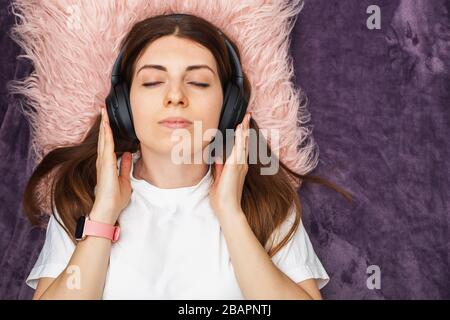 Jeune femme posée sur le lit et écoutant de la musique dans le casque Banque D'Images