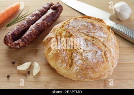 Pain de blé maison fraîchement cuit sur planche à découper en bois avec saucisse sèche, ail et épices. Cuisine gastronomique, saine, pâtisserie et régime alimentaire Banque D'Images