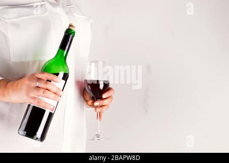 La femme tient un verre avec vin rouge et une bouteille de vin sur fond gris avec un espace de copie Banque D'Images