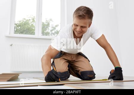 Professionnel artisan met stratifié dans un nouvel appartement. Le charpentier mesure la ligne de coupe sur le stratifié. Réparation du plancher en bois. Banque D'Images