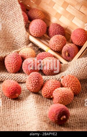 Vue en grand angle d'un panier incliné de fruits (Lichhi) de l'arbre lychee (Litchi chinensis) sur un tissu à grosses sackCloth dans un panier angulaire. Banque D'Images