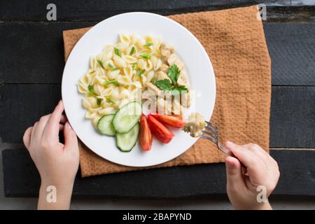 Tenir la fourchette pour manger des pâtes italiennes farfalle avec des tranches de légumes sur un fond en bois. Plat Banque D'Images