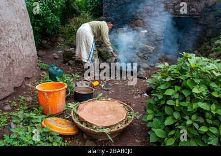 Femme cuisine Injera pancake comme du pain sur un mogogo au-dessus d'un feu. Lalibela, région d'Amhara, Ethiopie. Banque D'Images