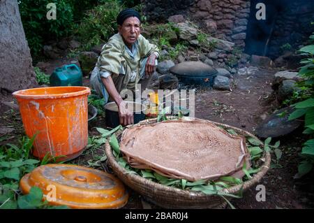 Femme cuisine Injera pancake comme du pain sur un mogogo au-dessus d'un feu. Lalibela, région d'Amhara, Ethiopie. Banque D'Images