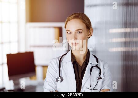 Une femme souriante et gaie se tenant debout avec les bras croisés dans la clinique. Portrait d'une femme médecin sympathique. Concept de médecine Banque D'Images